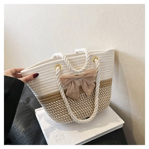 Detail of two-tone woven tote bag with rope handles and large beige bow ornament