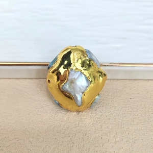 Detail of baroque pearl set in gold metal with blue-grey gemstones and textured finish