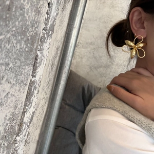 Macro detail of oversized gold-plated flower earrings worn to show size and artistic design
