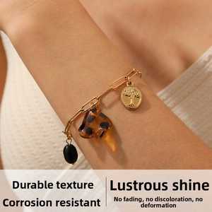 Detail of gold chain bracelet featuring tree of life pendant and leopard resin charm