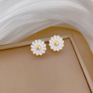 Macro detail of daisy floral earrings with white enamel petals and gold plating on jewelry box