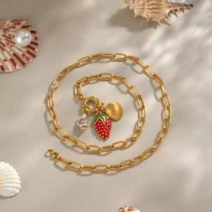 Collana in oro 18K con ciondoli a fragola e conchiglia su sfondo estetico da spiaggia