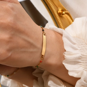 Detail shot of a golden cross-plate bracelet with colorful oil drip beads on a female wrist