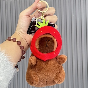 Pluche Capybara sleutelhanger met aardbeienhoed en gouden ring in de hand gehouden