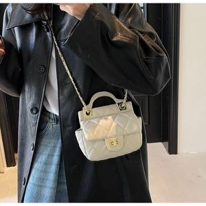 Detail of white quilted crossbody bag with gold twist lock and chain strap on a model