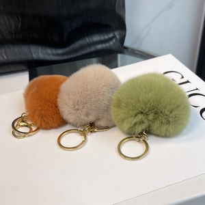 Close-up of three fluffy faux rabbit fur heart keychains in orange, beige, and sage green