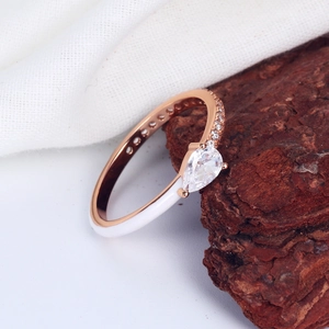 Macro shot of rose gold ring with pear-cut zircon and white enamel detail