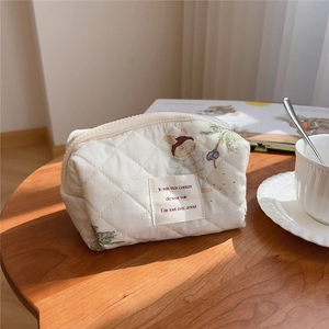 Detail of quilted cotton makeup bag with bear embroidery on a rustic wooden table