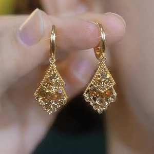 Detail of gold rhombus earrings with sparkling inlaid gems held by fingers