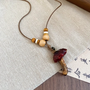 Close-up of a handmade red mushroom pendant necklace with wood beads on burlap background