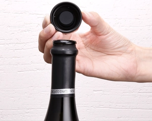 Detailed view of hand placing a black mini champagne stopper on a glass wine bottle