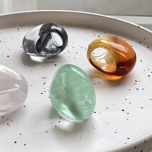 Minimalist oval resin rings in transparent, amber, and grey on a marble stone tray