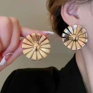Detail of oversized gold flower metal earrings shown on model and held by hand