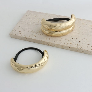 Close-up of golden metal hair tie with irregular hammered texture on white stone