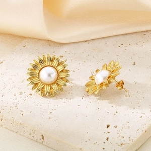 Macro shot of gold sunflower stud earrings with white pearl center on silk fabric