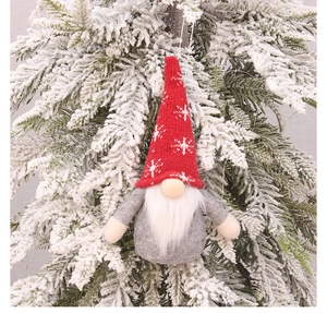 Detail of Christmas gnome plush with red knitted snowflake hat on snowy pine tree branch