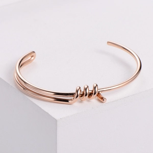 Minimalist rose gold stainless steel knot cuff bracelet on a white geometric display