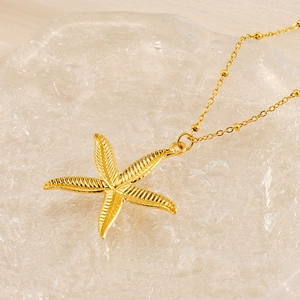 Golden starfish pendant necklace with textured detail and beaded chain on glass background