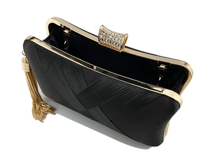 Detail of evening clutch featuring black textured fabric, gold fringe, and rhinestone clasp