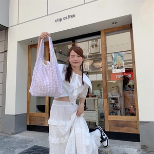 Detail view of the purple and white checkered canvas tote bag in a casual street setting
