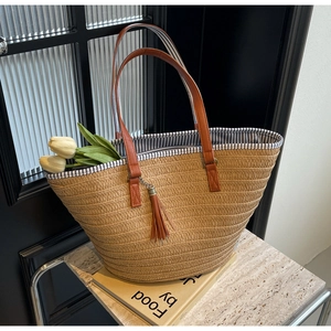 Detail of khaki woven straw tote bag with brown straps, tassels and blue striped lining