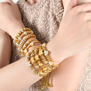 Stacked golden bead bracelets with butterfly charm and heart pendant on a wrist