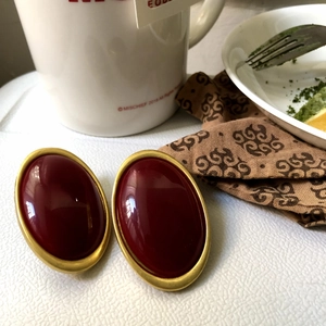 Close-up of retro oval dark red stud earrings with gold trim on a textured surface