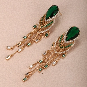 Macro detail of gold vintage earrings with emerald green pear-cut stones and tassels