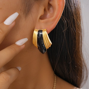 Close-up of gold geometric drop earring with black enamel and vertical textured metal