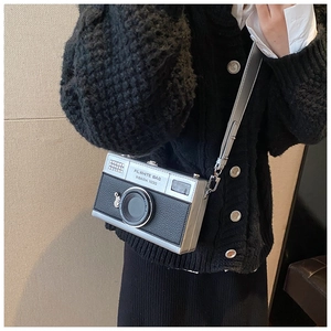 Detail of silver camera-shaped crossbody bag with Filwhite lettering on a black outfit