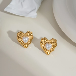 Detailed macro view of gold heart stud earrings with irregular texture and white pearl inlay
