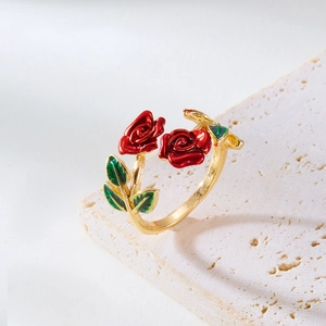 Detail of gold open ring with red and green enamel rose petals on marble stone