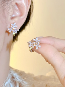 Close-up of lavender floral stud earrings with gold trim and green leaves worn on ear