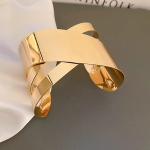 Dettaglio di un ampio bracciale a fascia dorato con design geometrico incrociato
