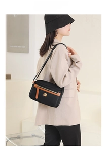 Detail of waterproof black nylon shoulder bag with brown leather trim worn in a cafe