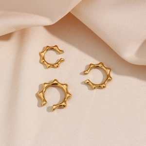 Detailed view of three gold polished 18K plated stainless steel ear cuffs on silk
