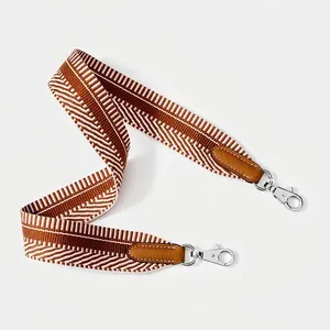 Close-up of a wide brown and white woven shoulder strap with silver swivel metal hooks