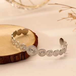 Detail of silver stainless steel open bangle with bohemian sunburst pattern coin charms