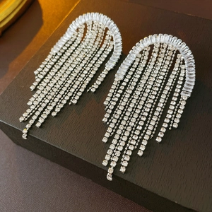 Close-up of silver long tassel earrings with sparkling rhinestones on dark wooden block