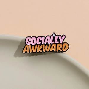 Socially Awkward enamel pin badge with pink and orange letters on a ceramic dish