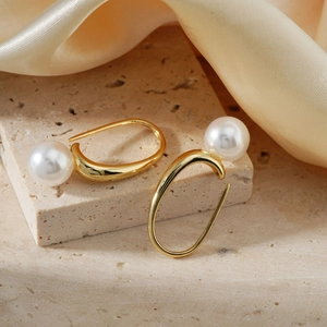 Élégantes boucles d'oreilles perles dorées avec perles blanches sur fond de pierre beige chic
