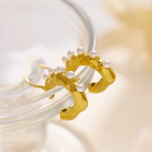 Macro shot of gold-plated wave-textured earrings with embedded small white pearls