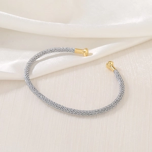 Detail of silver twisted metal cuff bracelet with golden ball ends on white silk