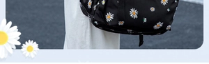 Detail of black nylon backpack with white daisy pattern worn by model against grey asphalt