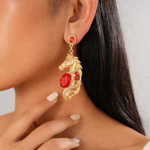 Close-up of golden horse head earrings with red gemstones and crystals on model