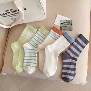 Détail de cinq paires de chaussettes en coton rayées colorées sur un coussin beige