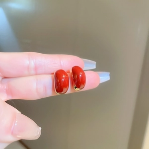 Detail of vintage gold-trimmed red enamel earrings held between fingers for size