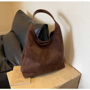 Detail of dark brown suede shoulder bag displayed on a stone surface with soft texture