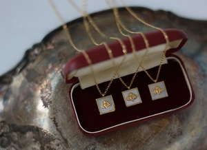 Detail of square bee relief pendant with white mother of pearl in red velvet jewelry box