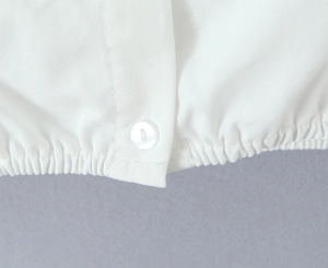 Detailed close-up of white twill fabric with elastic hem and matching round button